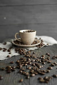 罗布斯塔摄影照片_亚麻纺织品和木桌上装满新鲜阿拉比卡或罗布斯塔咖啡豆的咖啡杯，咖啡豆散落。