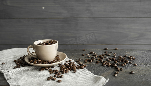 亚麻纺织品和木桌上装满新鲜阿拉比卡或罗布斯塔咖啡豆的咖啡杯，咖啡豆散落。