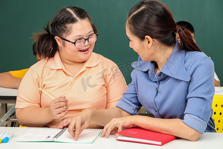 自闭症教育摄影照片_亚洲残疾儿童 或者，一名自闭症儿童在课桌前与老师一起学习阅读、写作和训练他们的手和手指肌肉。
