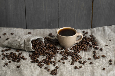 咖啡从亚麻布袋中散落，一杯黑咖啡浓咖啡或美式咖啡站在木桌上。