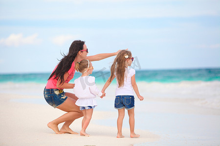 年轻的母亲和她可爱的女儿们在热带海滩享受暑假