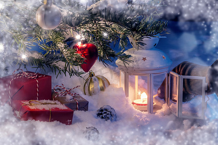 圣诞节手摄影照片_圣诞作文 — 雪中的树、礼物、装饰品和用火柴点燃灯笼的手