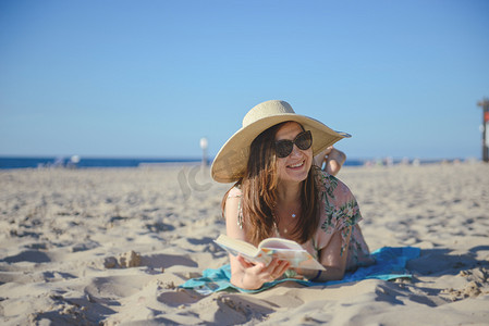书的海洋摄影照片_一个年轻的黑发女人在沙滩上放松的画像，正在阅读一本博