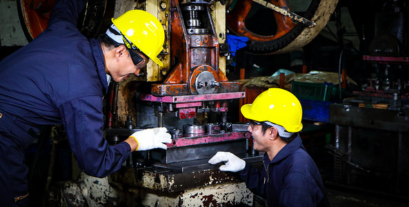 两名身着头盔制服的熟练亚裔工人正在讨论机器维修分析。