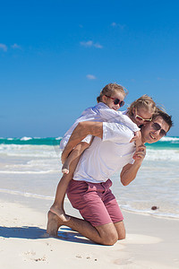 年轻爸爸和他可爱的女儿们在白色沙滩上玩得开心