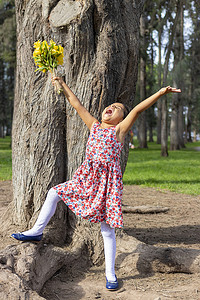 穿着裙子的小女孩手里拿着一束花在公园里庆祝