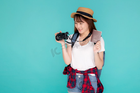 美丽的亚洲年轻女性肖像戴着帽子，微笑着自信地拿着护照和相机，在假期孤立的蓝色背景下带着护照和相机旅行，模范旅游亚洲女孩对旅程感到高兴。