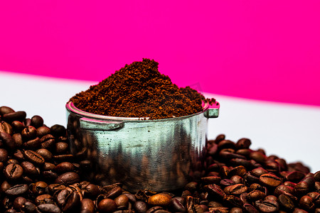咖啡与早餐摄影照片_咖啡豆和 portafilter 与磨碎的咖啡在粉红色背景上的组合。