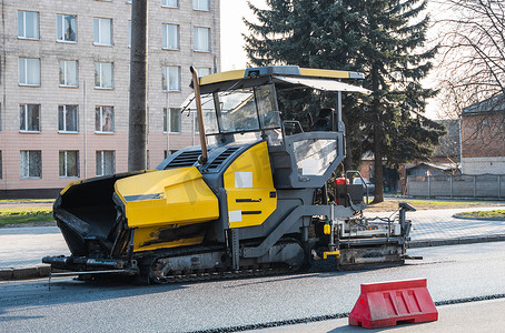 工业沥青摊铺机在街道道路施工现场铺设新鲜沥青。