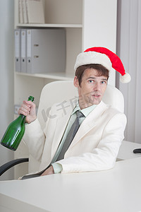 戴着圣诞帽的年轻人坐在桌边，手里拿着瓶子
