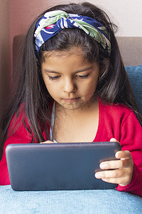 坐着的小女孩正在家里玩她的平板电脑