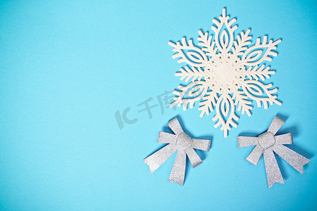 创意雪花摄影照片_白色闪闪发光的雪花和淡蓝色背景上的蝴蝶结