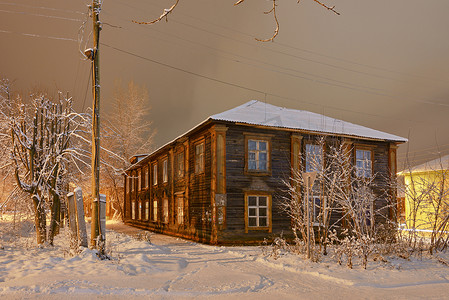 一条多雪的冷淡的街道上的老木房子在夜照明