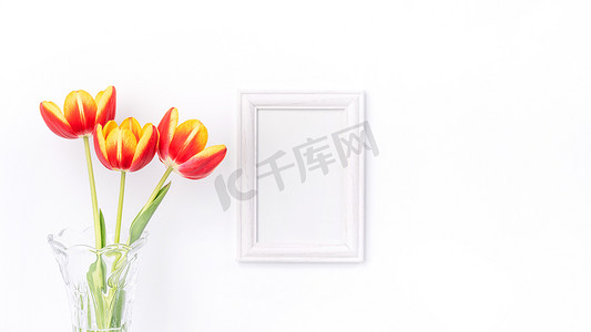 美丽的郁金香花在一个花瓶里，白墙上有相框装饰。
