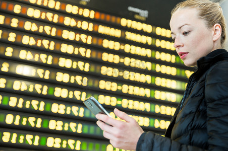 一位女士在机场的航班信息板前查看她的手机。