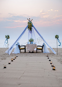 恩爱的情侣在沙滩上享用浪漫的晚餐，点着蜡烛、灯笼和酒杯，欣赏美妙的日落