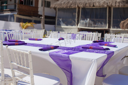 用紫色弓装饰的白色婚桌在沙滩