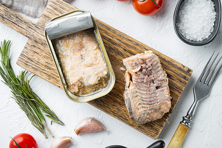 罐装野生阿拉斯加鲑鱼，放在木制切菜板上，白色背景，配有香草和配料，俯视平躺