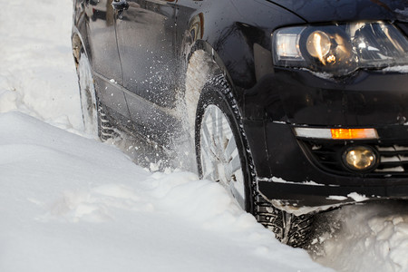 湿滑路面摄影照片_黑色车辆在深雪中行驶时打滑，车轮打滑并喷出积雪，它试图在湿滑的路面上获得牵引力。