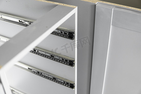 不锈钢伸缩卡口式抽屉滑轨，安装在灰色刨花板制成的厨柜上。