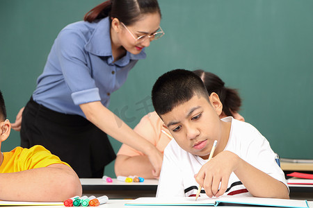 自闭症儿童展板摄影照片_亚洲残疾儿童 或者，一名自闭症儿童在课桌前与老师一起学习阅读、写作和训练他们的手和手指肌肉。