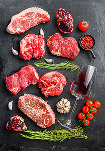 一套各种经典的、另类的生肉牛排，在黑色背景的顶视图上放着红酒。