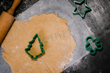 在深色背景的羊皮纸烘焙纸上，用生面团切出圣诞树形式的姜饼曲奇饼。