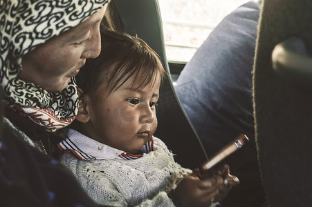 在一天的早晨，在父母节假期，一个藏族孩子坐在她母亲的膝上的特写。
