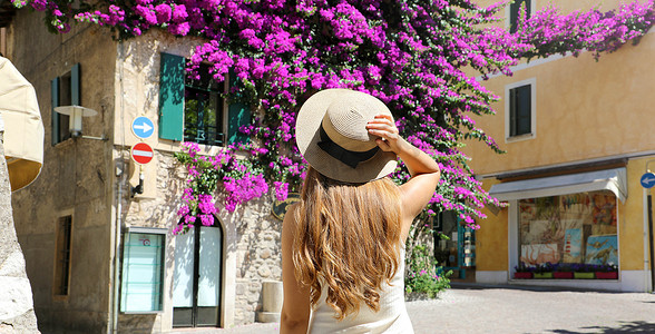年轻女游客戴着帽子参观意大利加尔达湖西尔苗内古镇的后景