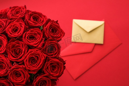 送玫瑰摄影照片_情人节的情书和送花服务、豪华的红玫瑰花束和红色背景的卡片信封