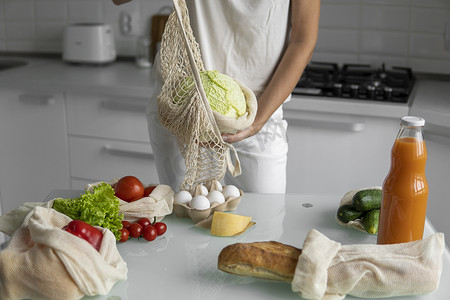 女人手拿着可重复使用的生态纺织品购物袋和蔬菜，把卷心菜拿出来。