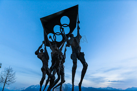 瑞士洛桑-2016 年 11 月 12 日-背景为蓝天的沃州莱蒙湖岸奥林匹克博物馆前手持奥林匹克运动会五环标志的雕塑