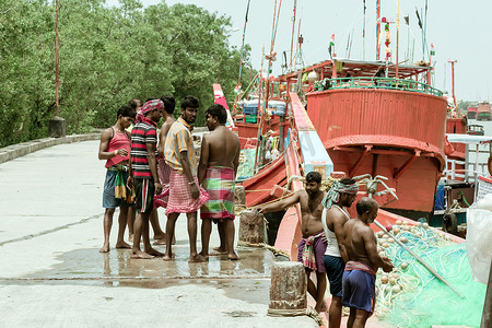 印度农村渔民社区站在沿海贫困地区渔村的渔船附近，然后驶向河海捕鱼。