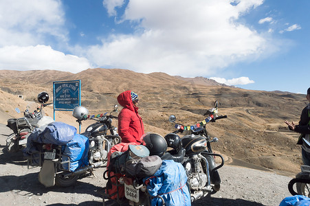 印度女性旅行者徒步旅行者和骑自行车的人站在她的摩托车旁边，远足高喜马拉雅山地区郊游和探索当地的山站。