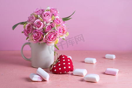 淡彩玫瑰摄影照片_白色和粉色的小棉花糖散落在淡粉色的背景上，旁边是一瓶玫瑰。
