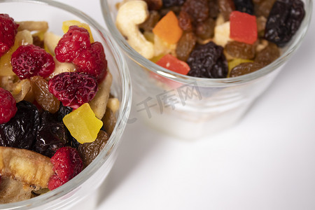 muesli 甜点配酸奶和蜜饯或干果，顶部有覆盆子，玻璃杯隔离在白色背景上。