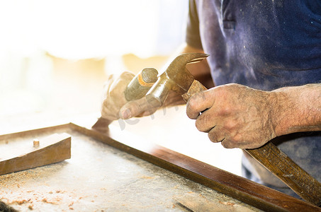 在木制工作台上用凿子和锤子工作的木匠手的特写