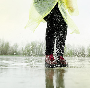 女人在雨中玩耍，在溅起的水坑中跳跃