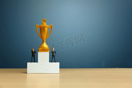 领奖摄影照片_微型商业概念 — 商人站在白人领奖台前，拿着金奖杯