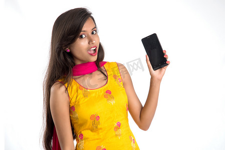 年轻漂亮的女人拿着并在白色背景上展示空白屏幕智能手机或手机或平板电脑。