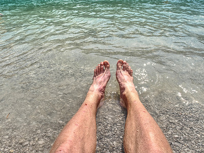蓝绿色摄影照片_多毛的强壮男性腿在山湖冷水中冷却