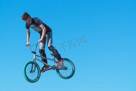 年轻的 BMX 骑自行车的人，在 BMX 上有腿保护，在背景天空中做空中特技