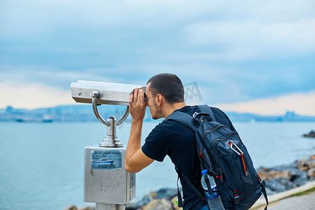 望远镜观星插画摄影照片_一个背着背包的旅游者透过观景台上的观光双筒望远镜望去