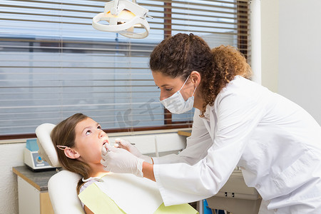 牙医椅摄影照片_儿科牙医在牙医椅上检查病人的牙齿