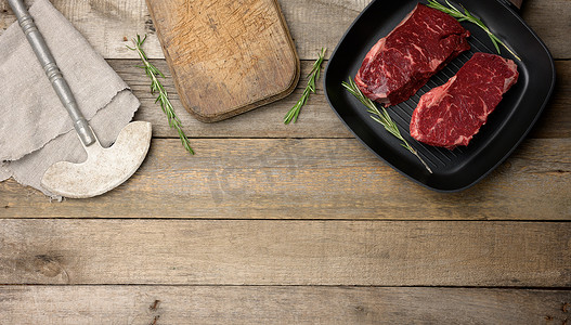黑色方形烤盘里的两块生牛肉，木桌上的切板和刀