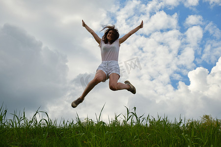 跳跃以蓝天和云彩为背景的愉快的女孩