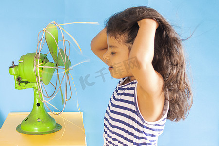 空气降温摄影照片_美丽的女孩，正在用一把旧的绿色风扇降温