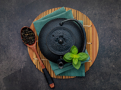 黑色铸铁茶壶，配以深色石头背景的凉茶。