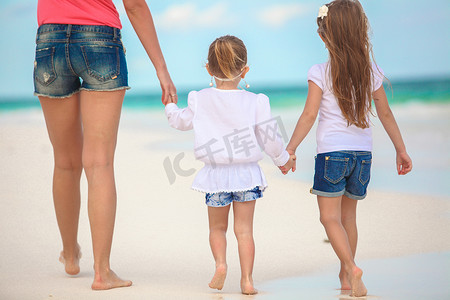 年轻母亲和她可爱的女儿们在海边散步的背影