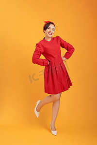 身穿红色连衣裙的年轻 gorgoeus 亚洲女性站在橙色背景上。